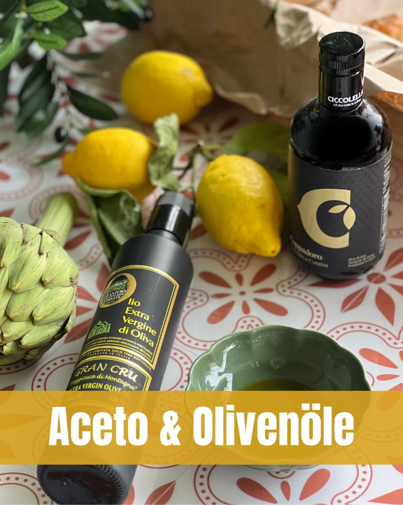 Eine Zusammenstellung von zwei edlen, schwarzen Flaschen (links das Frantoio d’Oneglia Olivenöl, rechts das Ciccolella Aceto/Öl), flankiert von einer frischen Artischocke und drei Zitronen auf einem gemusterten Tisch. Eine kleine, gewellte, grüne Schale mit Olivenöl steht davor. Ein gelbes Textbanner im Vordergrund trägt den weißen Schriftzug "Aceto & Olivenöle".