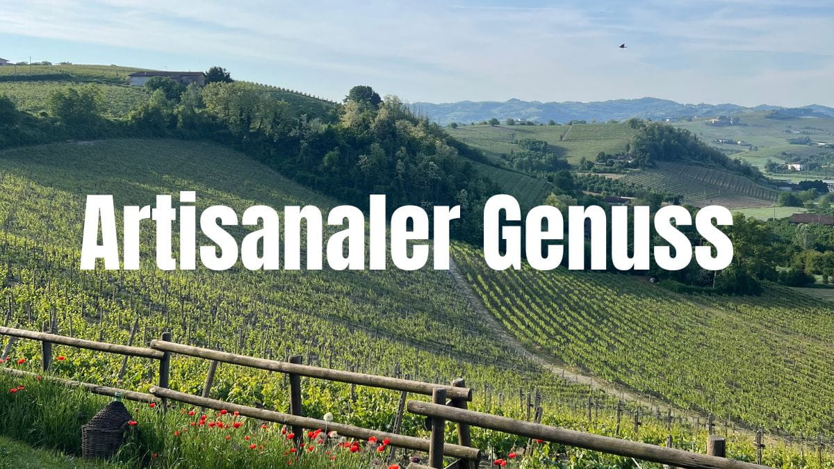 Eine hügelige Weinlandschaft im Sonnenschein mit grünen Reben, einem Holzzaun mit roten Mohnblumen im Vordergrund und dem großen weißen Schriftzug „Artisanaler Genuss“ in der Mitte des Bildes.
