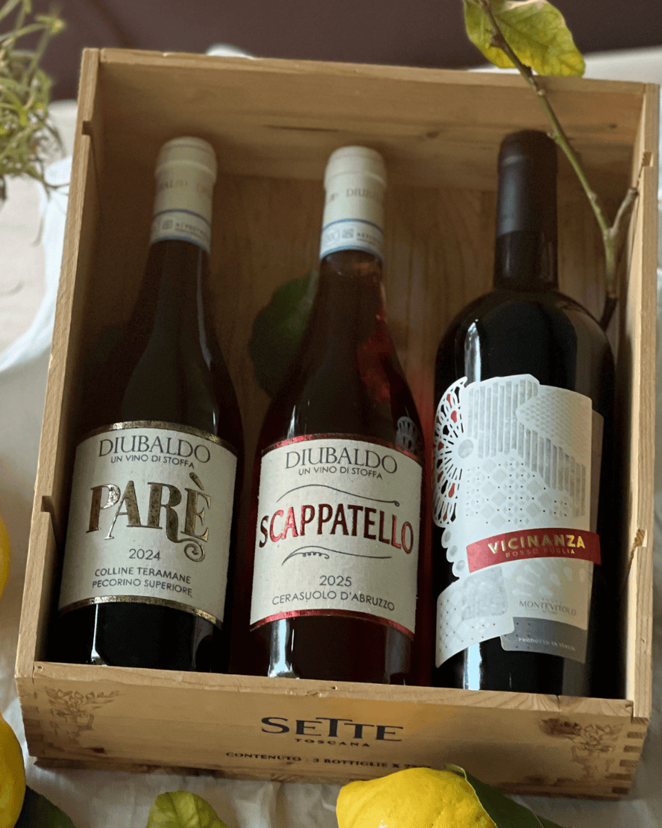 Holzkiste mit italienischen Bio-Weinen: Pecorino d’Abruzzo, Cerasuolo d’Abruzzo und Rosso Puglia IGT, dekoriert mit Zitronen und grünen Blättern im mediterranen Stil.